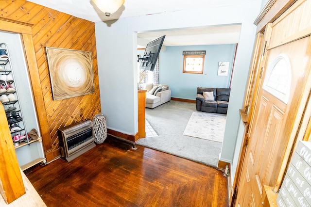 foyer entrance featuring baseboards, heating unit, wood walls, and wood finished floors