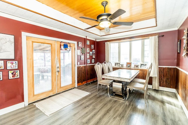 dining space featuring wood walls, wainscoting, and a raised ceiling