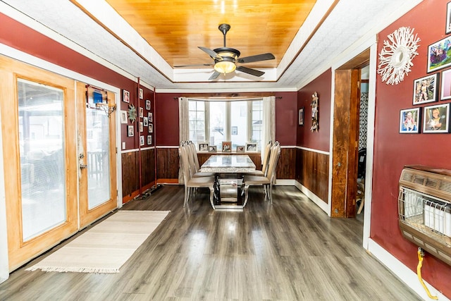 dining room featuring heating unit, a tray ceiling, wood finished floors, and wainscoting