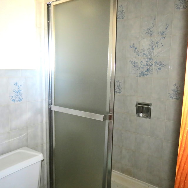 bathroom featuring toilet, tile walls, and a shower stall