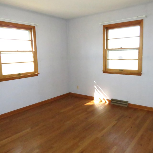 unfurnished room with wood finished floors, visible vents, and baseboards