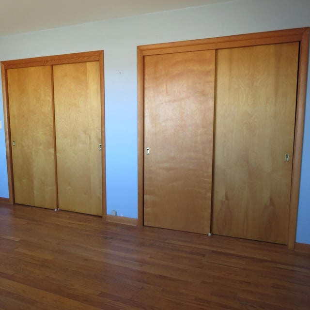 unfurnished bedroom with baseboards, multiple closets, and wood finished floors