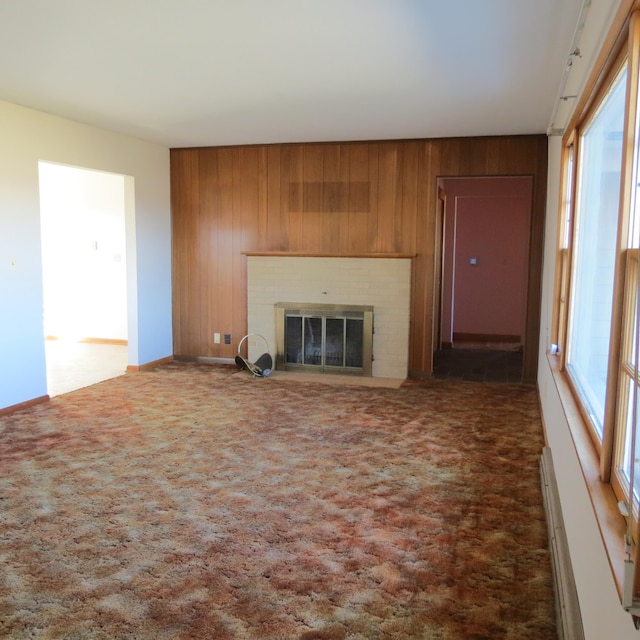 unfurnished living room with a brick fireplace, carpet flooring, and wooden walls