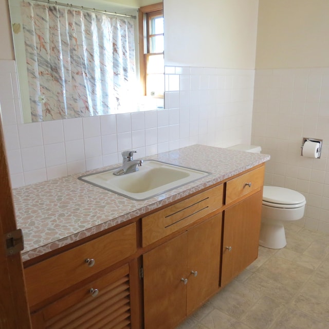 bathroom with tile walls, wainscoting, toilet, and vanity