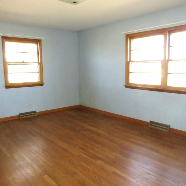 unfurnished room featuring visible vents, plenty of natural light, and wood finished floors