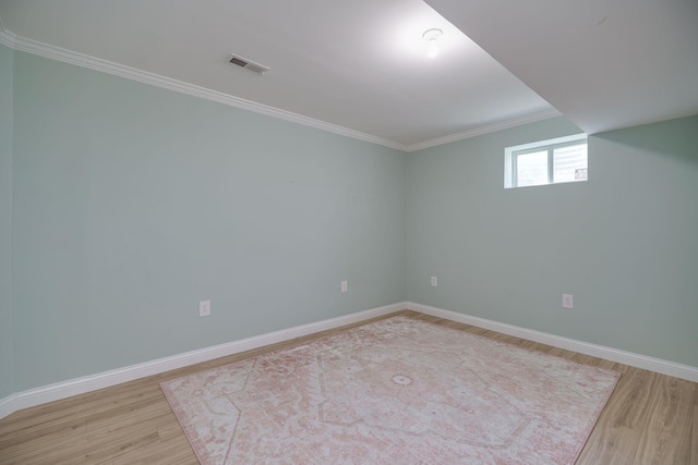 empty room featuring baseboards, visible vents, light wood-style floors, and crown molding