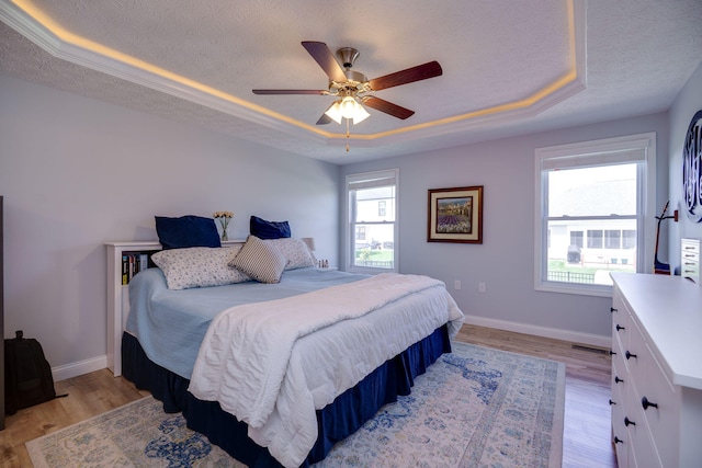 bedroom featuring baseboards, a tray ceiling, a textured ceiling, and light wood-style floors