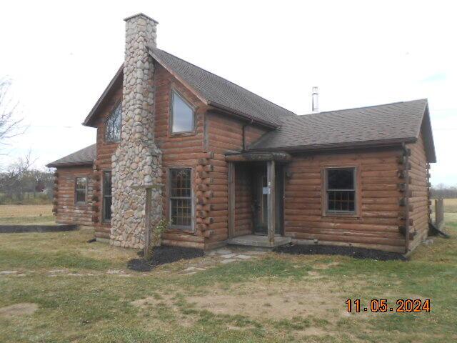 view of front facade with a front yard, log exterior, roof with shingles, and a chimney