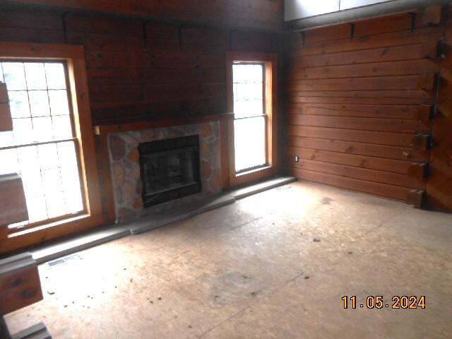 unfurnished living room featuring a stone fireplace, a healthy amount of sunlight, and wooden walls