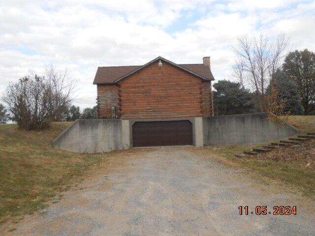 view of side of property with an attached garage, a chimney, log exterior, and driveway