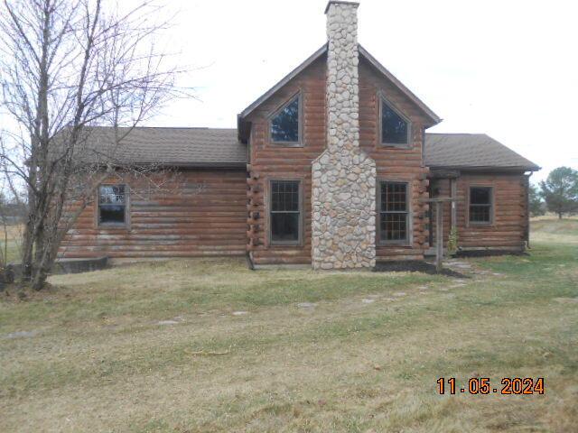 rear view of property with a yard, roof with shingles, log exterior, and a chimney