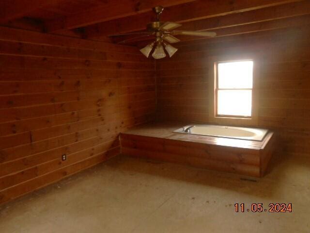 interior space with ceiling fan, wooden walls, and a bath