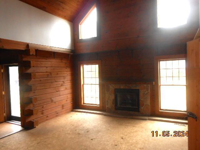 unfurnished living room with wooden walls, high vaulted ceiling, wood ceiling, and a fireplace