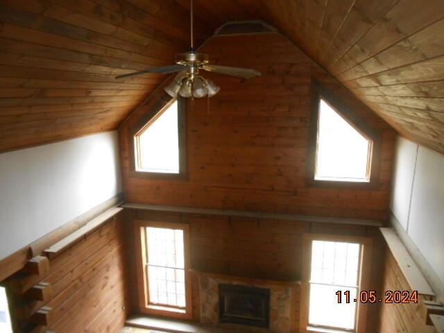 interior space with wooden ceiling, a large fireplace, ceiling fan, and vaulted ceiling