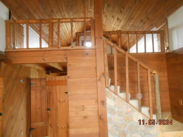 staircase with plenty of natural light, wood walls, wooden ceiling, and vaulted ceiling