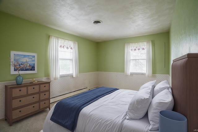 bedroom with multiple windows, a baseboard heating unit, and light carpet