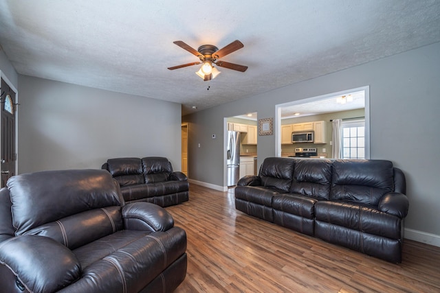 living area with a ceiling fan, a textured ceiling, baseboards, and wood finished floors