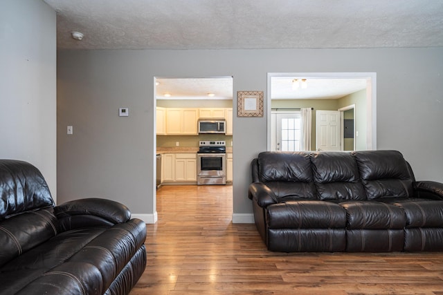 living room featuring a textured ceiling, baseboards, and wood finished floors