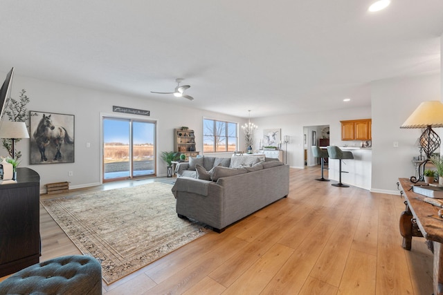 living room with ceiling fan with notable chandelier and light wood-type flooring