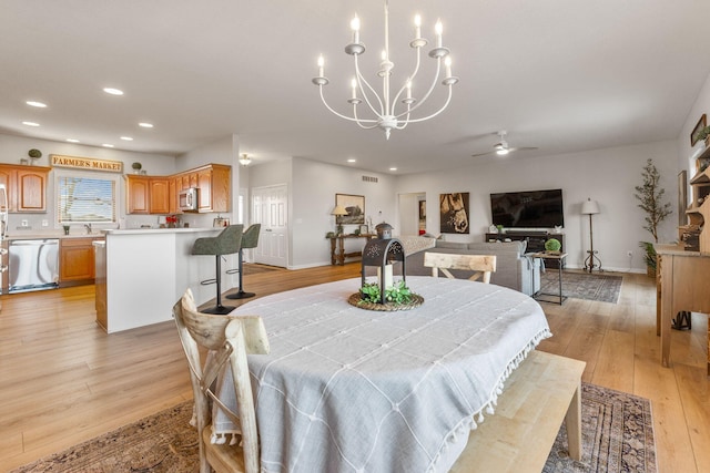 dining area with sink, ceiling fan with notable chandelier, and light hardwood / wood-style flooring