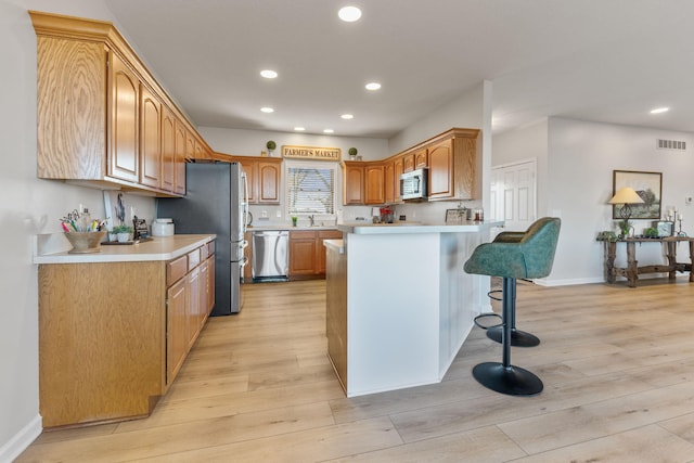 kitchen with sink, stainless steel appliances, light hardwood / wood-style floors, a kitchen bar, and kitchen peninsula