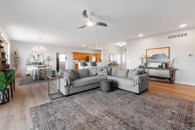 living room with ceiling fan with notable chandelier and light wood-type flooring