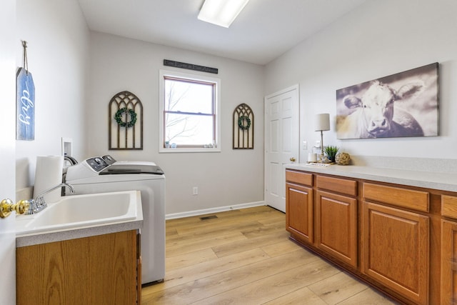 laundry room featuring cabinets, washer and clothes dryer, sink, and light wood-type flooring