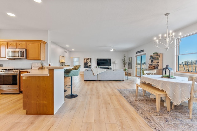 kitchen featuring decorative light fixtures, a breakfast bar area, kitchen peninsula, stainless steel appliances, and light hardwood / wood-style flooring