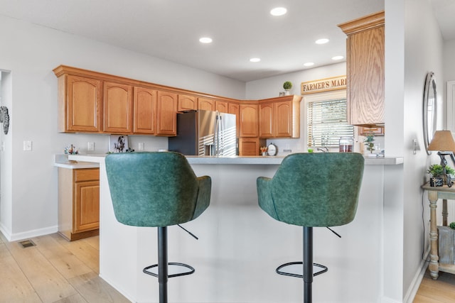 kitchen featuring a breakfast bar, stainless steel fridge, light wood-type flooring, and kitchen peninsula