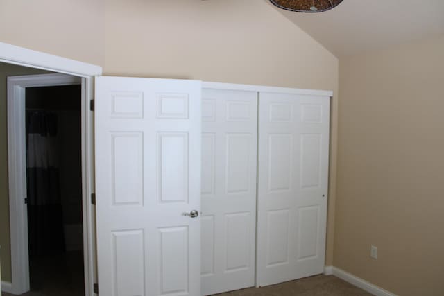 unfurnished bedroom with lofted ceiling, a closet, carpet flooring, and baseboards