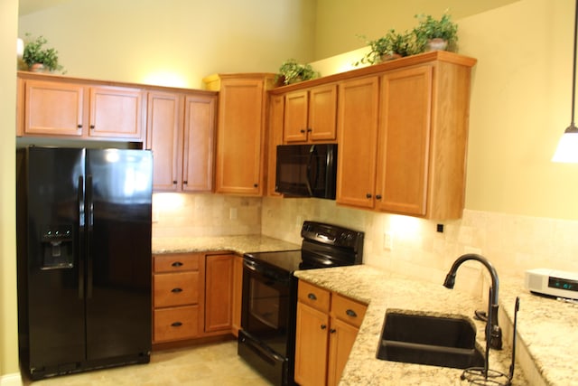 kitchen with black appliances, light stone counters, and a sink