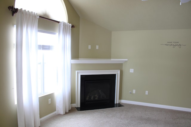 unfurnished living room featuring a fireplace with flush hearth, lofted ceiling, baseboards, and carpet