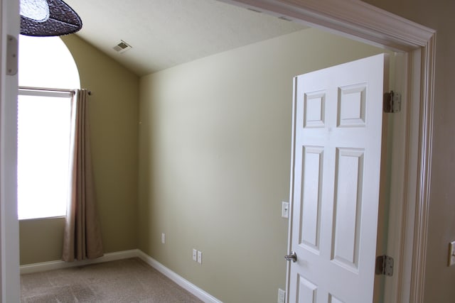 unfurnished room featuring vaulted ceiling, baseboards, visible vents, and light colored carpet