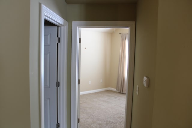 corridor with baseboards and light colored carpet