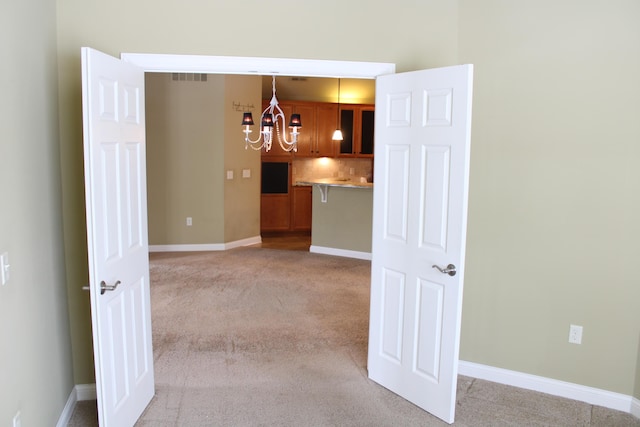 spare room featuring baseboards, an inviting chandelier, and light colored carpet