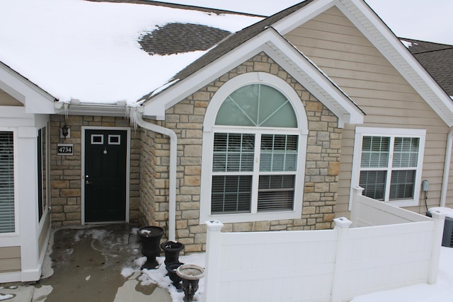 entrance to property with a shingled roof and stone siding