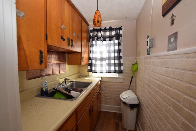 kitchen featuring a textured ceiling, a wainscoted wall, a sink, light countertops, and brown cabinetry