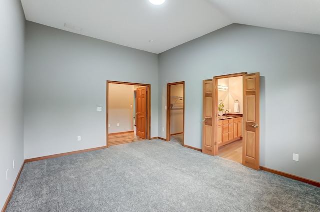 unfurnished bedroom with a closet, light colored carpet, a spacious closet, ensuite bath, and baseboards