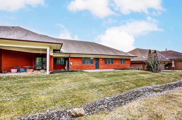 rear view of house with a yard, a patio, and a shingled roof