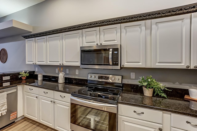 kitchen featuring dark stone counters, appliances with stainless steel finishes, light wood finished floors, and white cabinetry