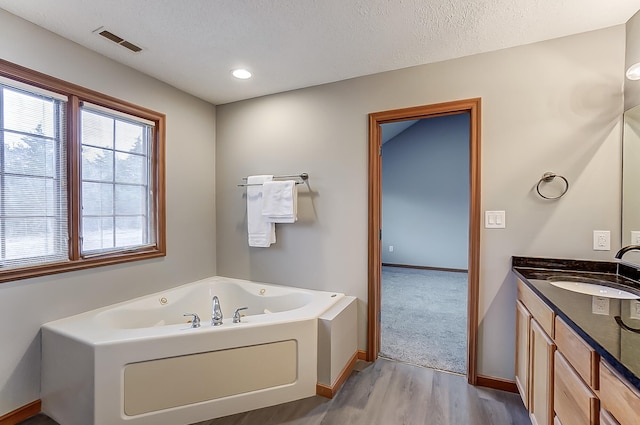 full bath featuring baseboards, visible vents, a whirlpool tub, a textured ceiling, and vanity