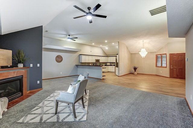 living area featuring lofted ceiling, visible vents, baseboards, light wood-type flooring, and a glass covered fireplace