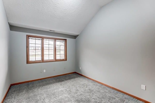 spare room featuring a textured ceiling, lofted ceiling, carpet floors, visible vents, and baseboards