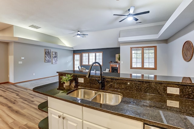 kitchen featuring light wood finished floors, visible vents, a ceiling fan, a sink, and dark stone counters