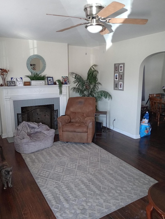 living room featuring a ceiling fan, arched walkways, a fireplace, and wood finished floors