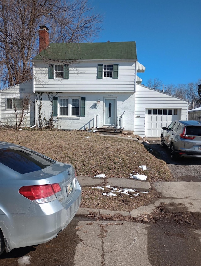 colonial home with aphalt driveway, a chimney, and an attached garage