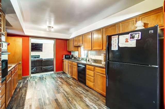 kitchen with dark wood-type flooring, a sink, black appliances, brown cabinetry, and dark countertops