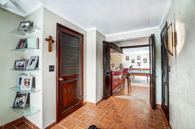 hallway with baseboards, a textured wall, ornamental molding, and stone tile floors