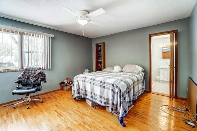 bedroom featuring baseboards, ceiling fan, ensuite bathroom, a textured ceiling, and light wood-type flooring