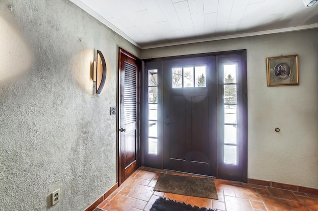 foyer featuring stone tile flooring, a textured wall, and baseboards